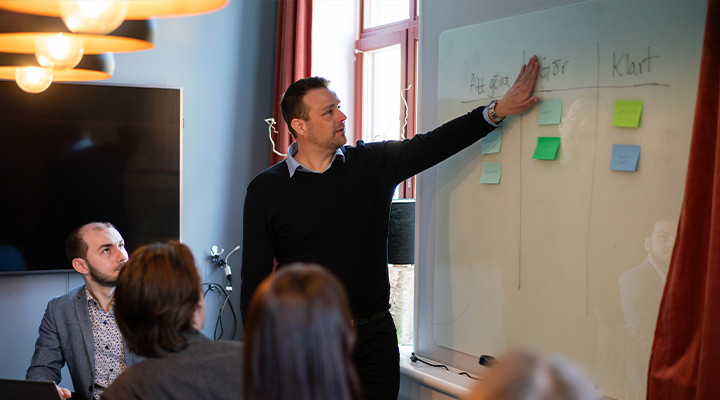 Person håller i arbetsmöte, sätter post-its på tavla