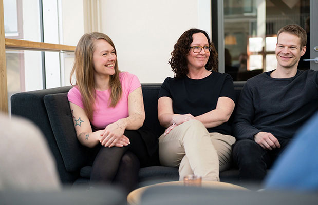 Tre glada personer sitter i en soffa och pratar.