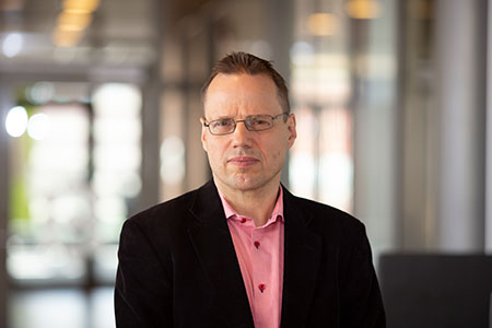 Erik Janzon klädd i glasögon, mörkrosa skjorta och svart kavaj.