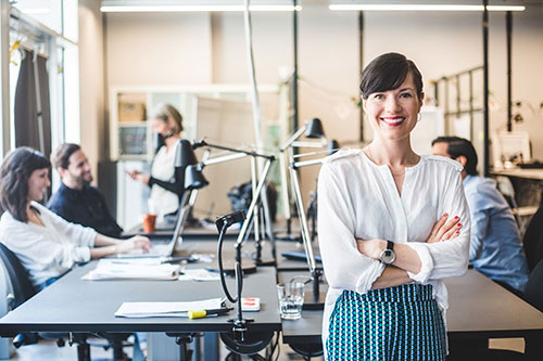 En kvinna står framför ett bord i ett mötesrum där det sitter fler personer.