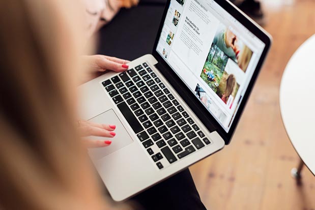 Person med rödmålade naglar använder en bärbar dator med bilder och text på skärmen.