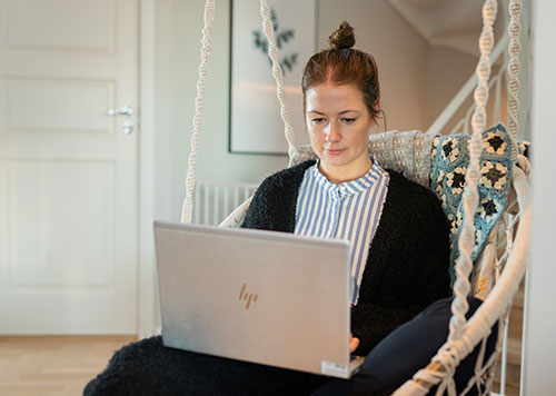 Kvinna sitter i rottingstol med en laptop i sitt knä.
