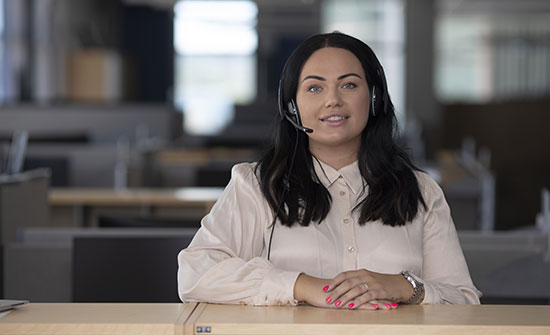 En person i ljus tröja står vid ett bord och pratar i sitt headset.