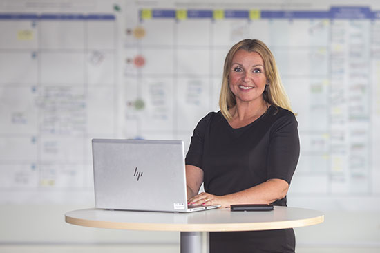 En glad person i en svart tröja står och jobbar på en laptop.