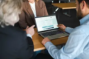 Tre personer sitter vid en dator under ett möte.