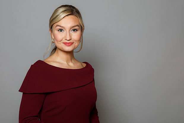 Ebba Busch står framför grå vägg. Har röd outfit.