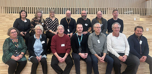 Gruppbild på 14 personer som sitter ner i två rader och ler mot kameran.