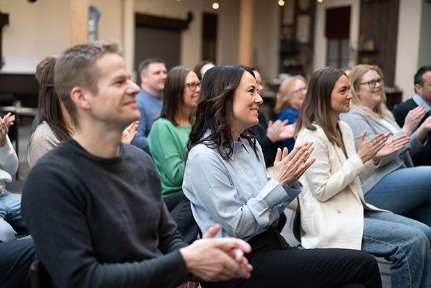Glada personer sitter i en publik och applåderar.