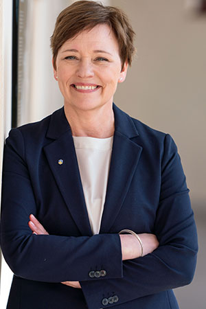 Inga Otmalm klädd i vit topp och en mörkblå kavaj ler mot kameran.