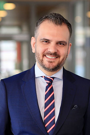 Dani Dawoodson klädd i ljus skjorta, mörkblå kavaj och en randig slips, ler mot kameran.