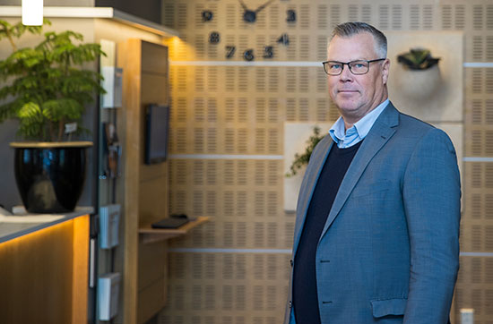 Tomas Lindfors klädd i ljusblå skjorta, mörkblå tröja och en mellanblå kavaj. Bakgrunden visar en del av Bolagsverkets reception.