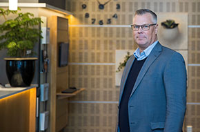Tomas Lindfors klädd i ljusblå skjorta, mörkblå tröja och en mellanblå kavaj. Bakgrunden visar en del av Bolagsverkets reception.