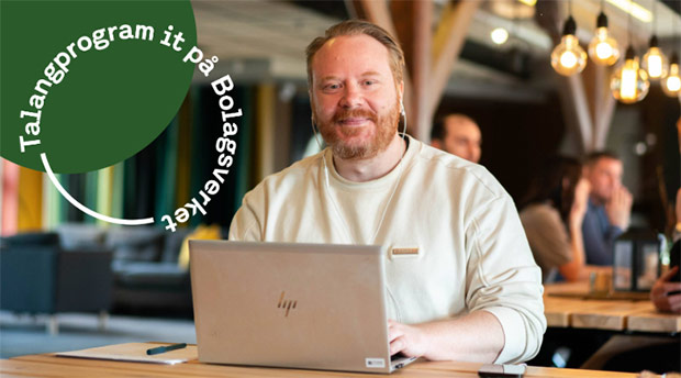 En man sitter vid ett bord och arbetar på en bärbar dator i en miljö som liknar ett café eller kontor. Han ler mot kameran. I bilden finns även en grafisk cirkel med texten ”Talangprogram it på Bolagsverket”.