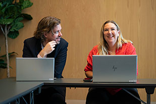 Två personer sitter vid ett bord och samtalar. De har en bärbar dator.