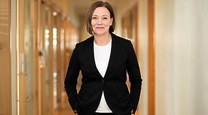 Inga Otmalm står i en korridor på Bolagsverket. Iförd svart kavaj och vit tröja.