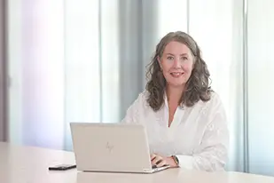 En person i vit blus sitter framför en dator i ett ljust rum.