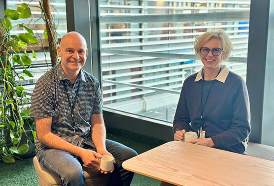 Två personer sitter vid ett bord och har var sin kopp i handen och ler mot kameran.