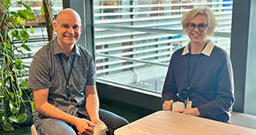 Två personer sitter vid ett bord och har var sin kopp i handen och ler mot kameran.