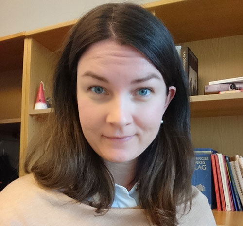 Lina Bjersbo står framför en bokhylla och ler mot kameran.