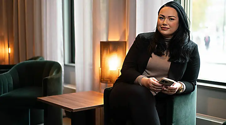 En person sitter avslappnat i en fåtölj med en telefon i handen.