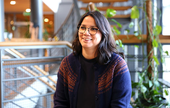 En person står i utomhusmiljö, klädd i en mönstrad halsduk och en mörkblå täckjacka.