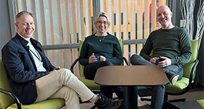 It-produktions sektionschefer sitter avslappnat i gröna fåtöljer runt ett bord med en kopp kaffe i händerna. 