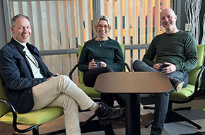 It-produktions sektionschefer sitter avslappnat i gröna fåtöljer runt ett bord med en kopp kaffe i händerna. 