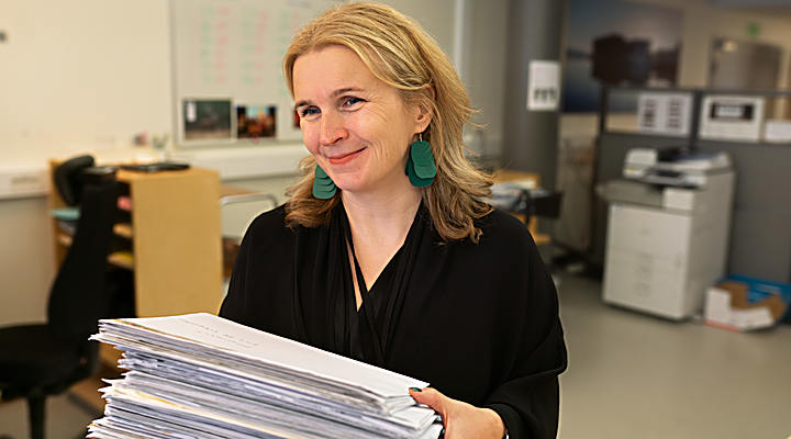 En person står och har en stor bunt papper i sina händer.