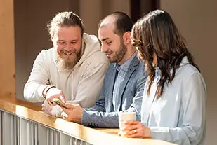 Tre glada personer sitter i en soffa och pratar.