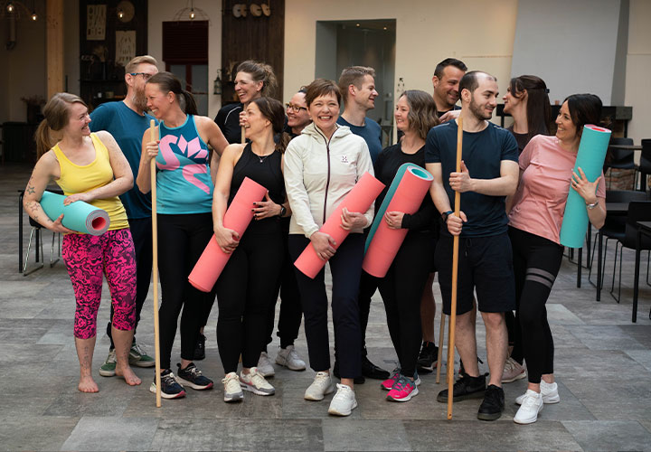 Gruppbild på medarbetare i träningskläder, som håller i yogamattor och pinnar.