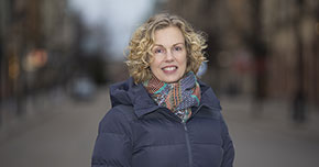 Kvinna med lockigt hår och färgglad halsduk står utomhus på en gata.