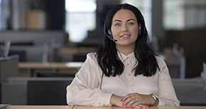 Kvinna med headset sitter vid ett skrivbord i ett kontorslandskap.