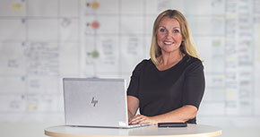 Leende kvinna vid ett runt bord med en bärbar dator framför sig.